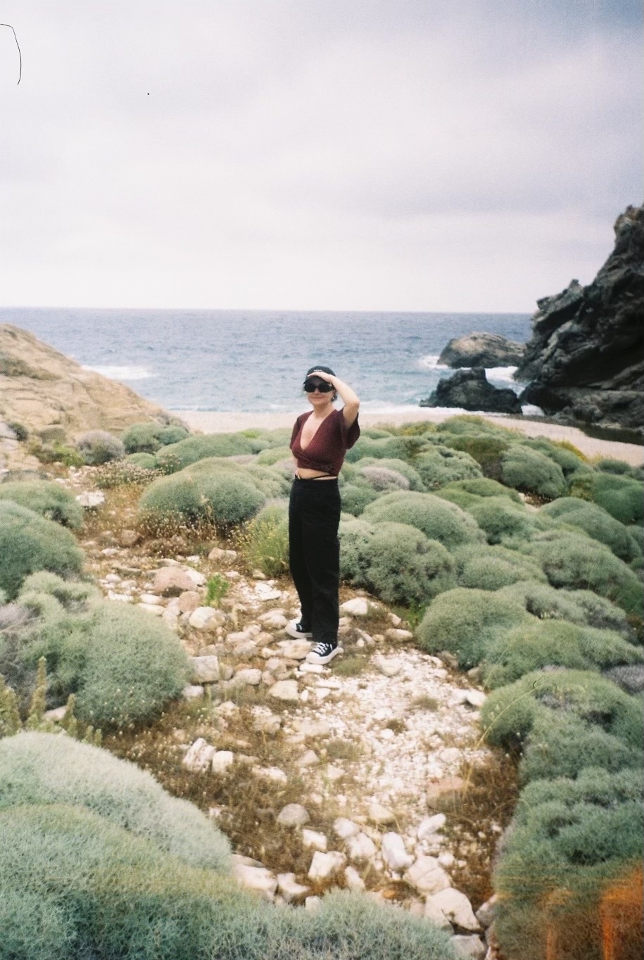 Anastasia Pachni Tsitiridou standing among sage green shrubs by the sea